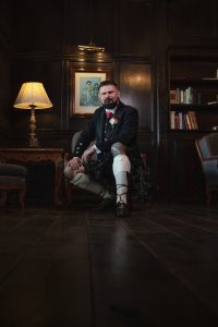 Groom wearing a tartan kilt seated in a wood-panelled room at Webbington Hotel